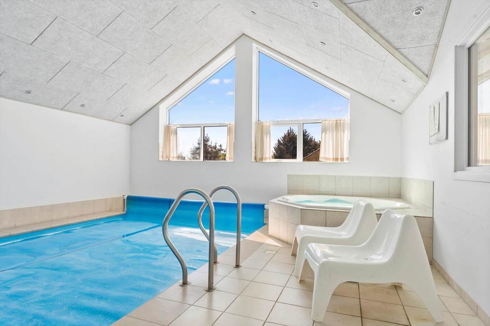 Indoor pool with hot tub and seating under high ceiling with large windows.