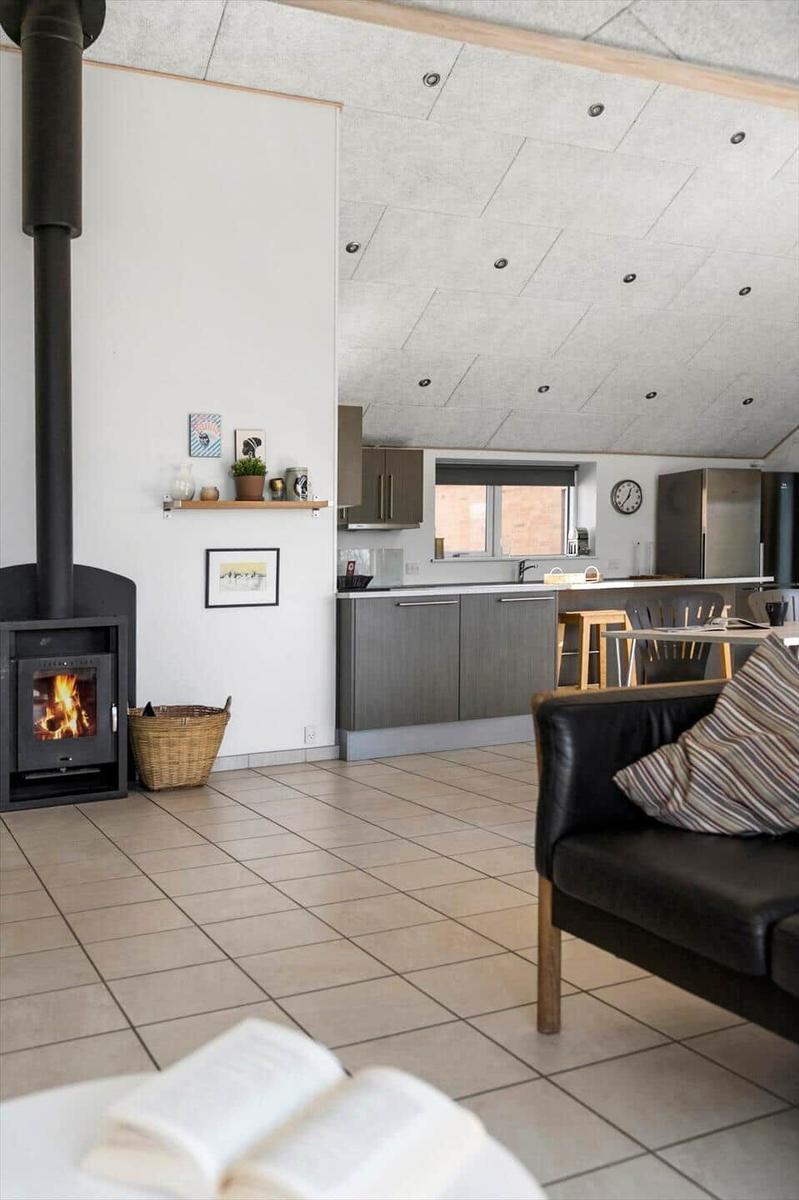Living area with wood stove, kitchen, and seating. Wooden floor and light walls.