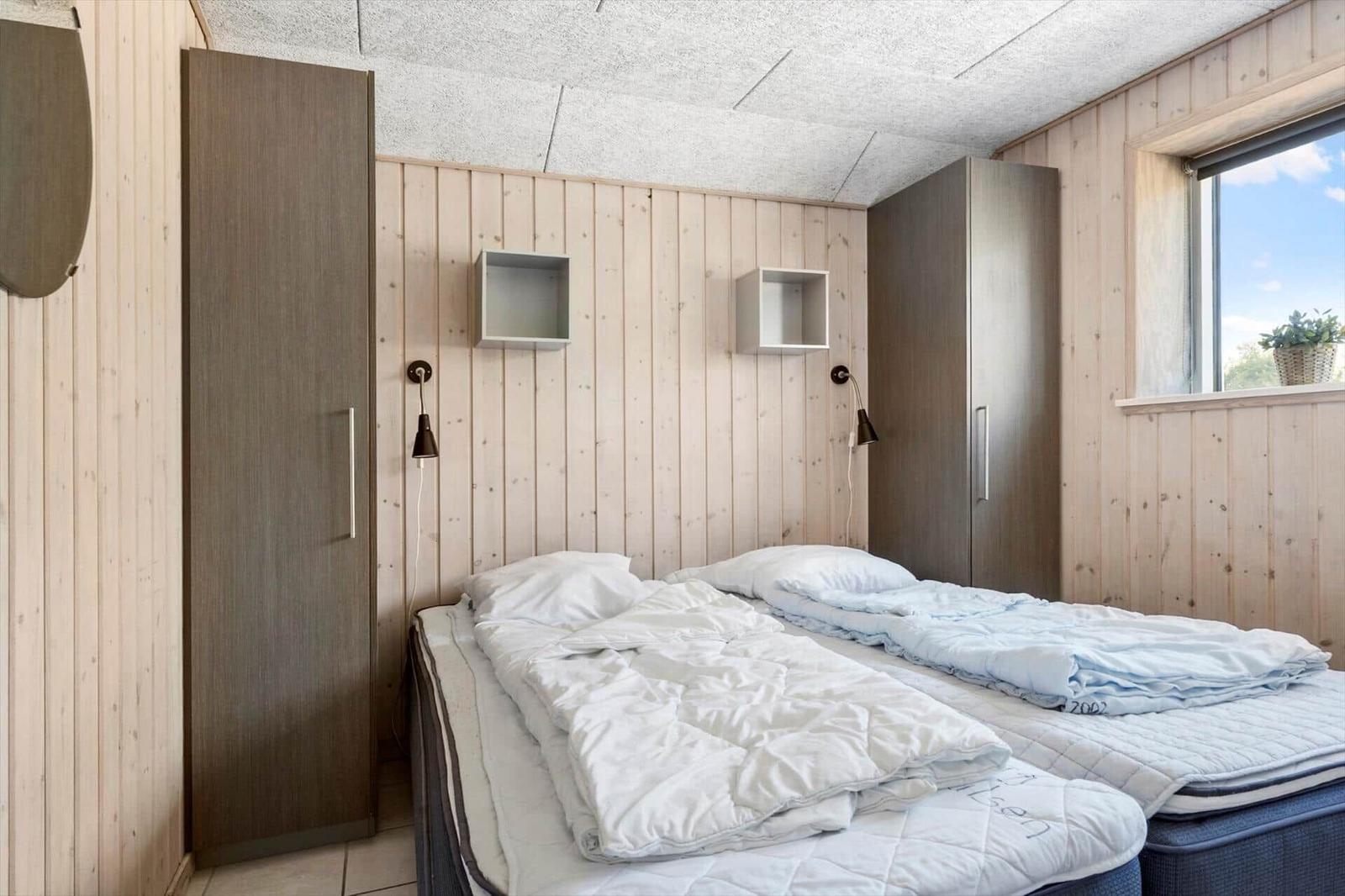 Two beds with white bedding, wood walls, and window with plant.