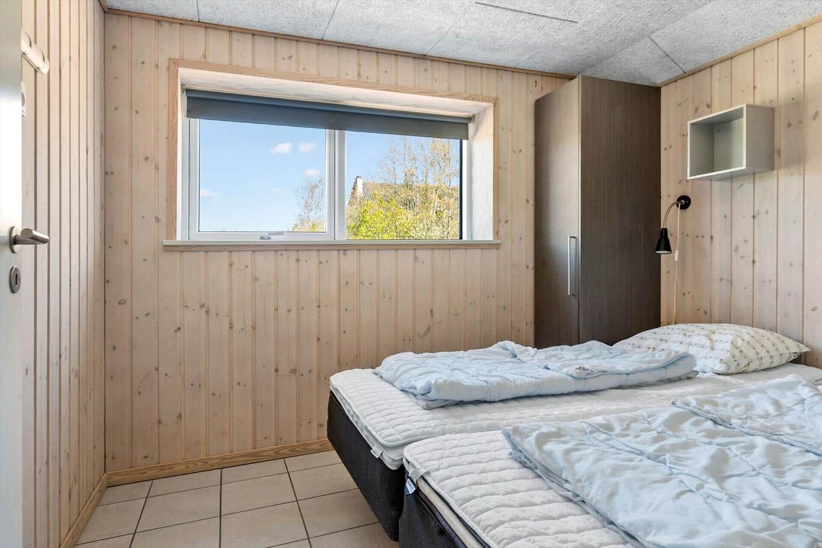 Room with two beds, wooden walls, and window with view of greenery.