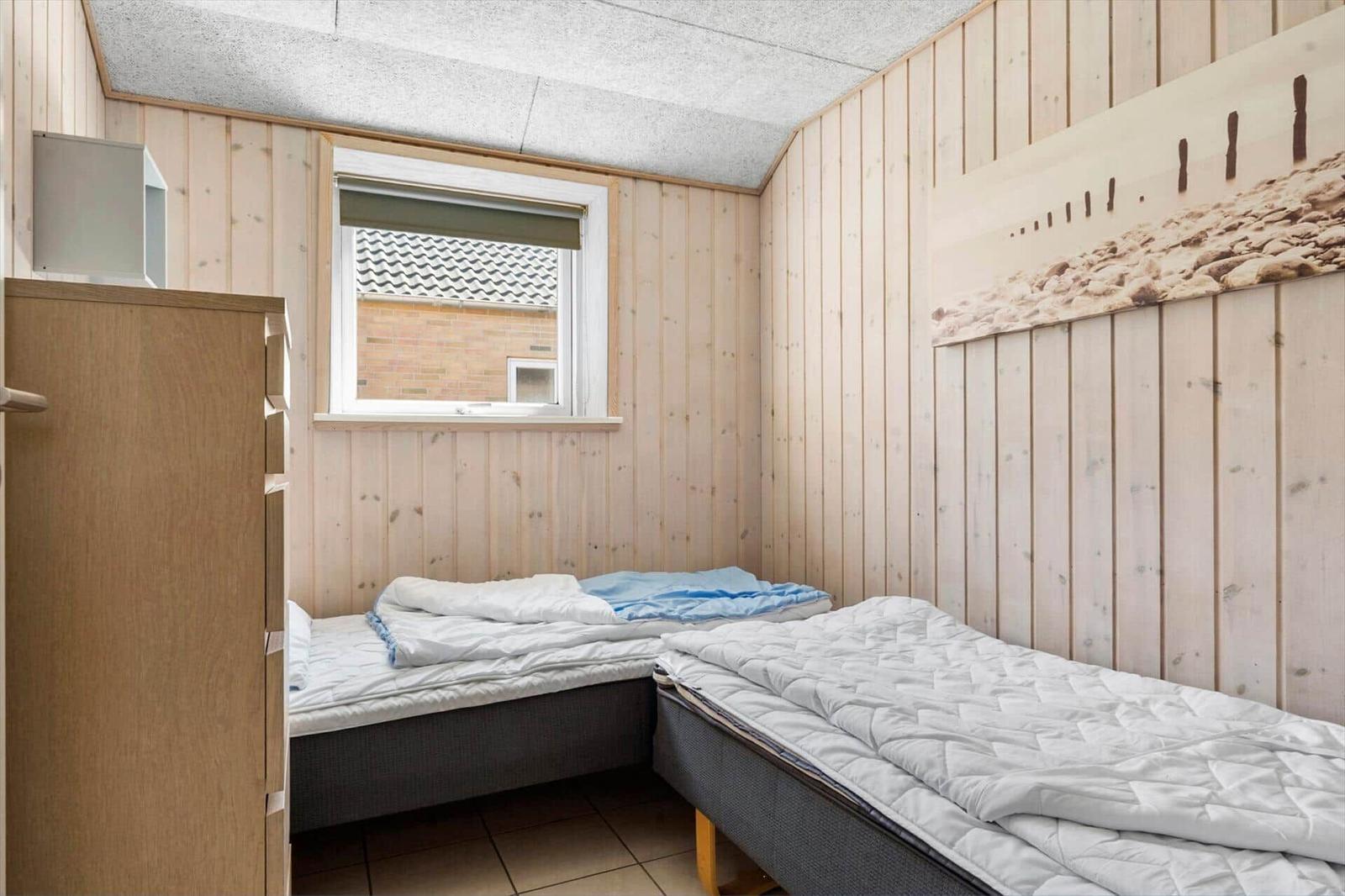 Room with two beds, wood-paneled walls, and window with view of exterior.