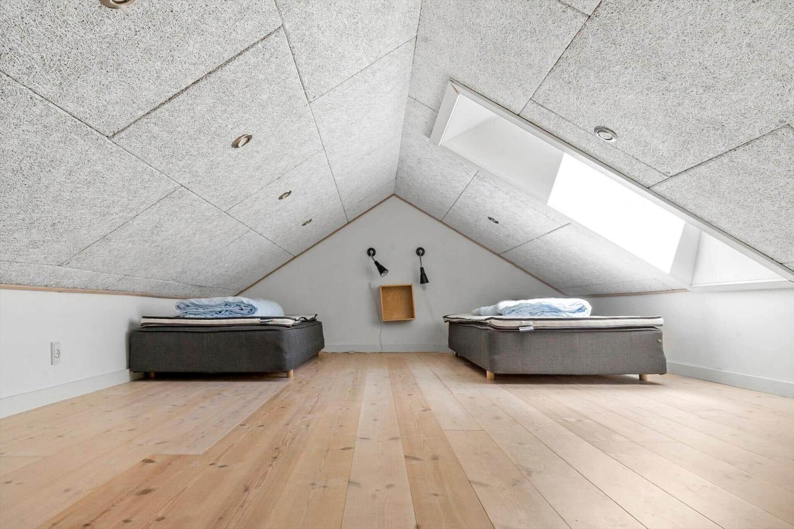 Two beds under a sloped ceiling with wooden floor and skylight.