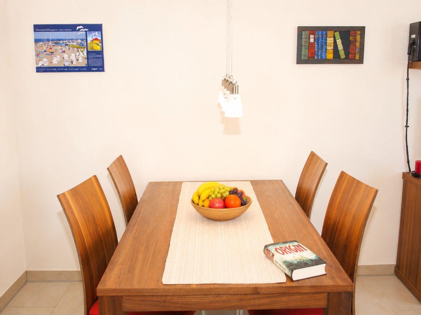 Holztisch mit vier Stühlen, Obstschale und Buch auf Tisch