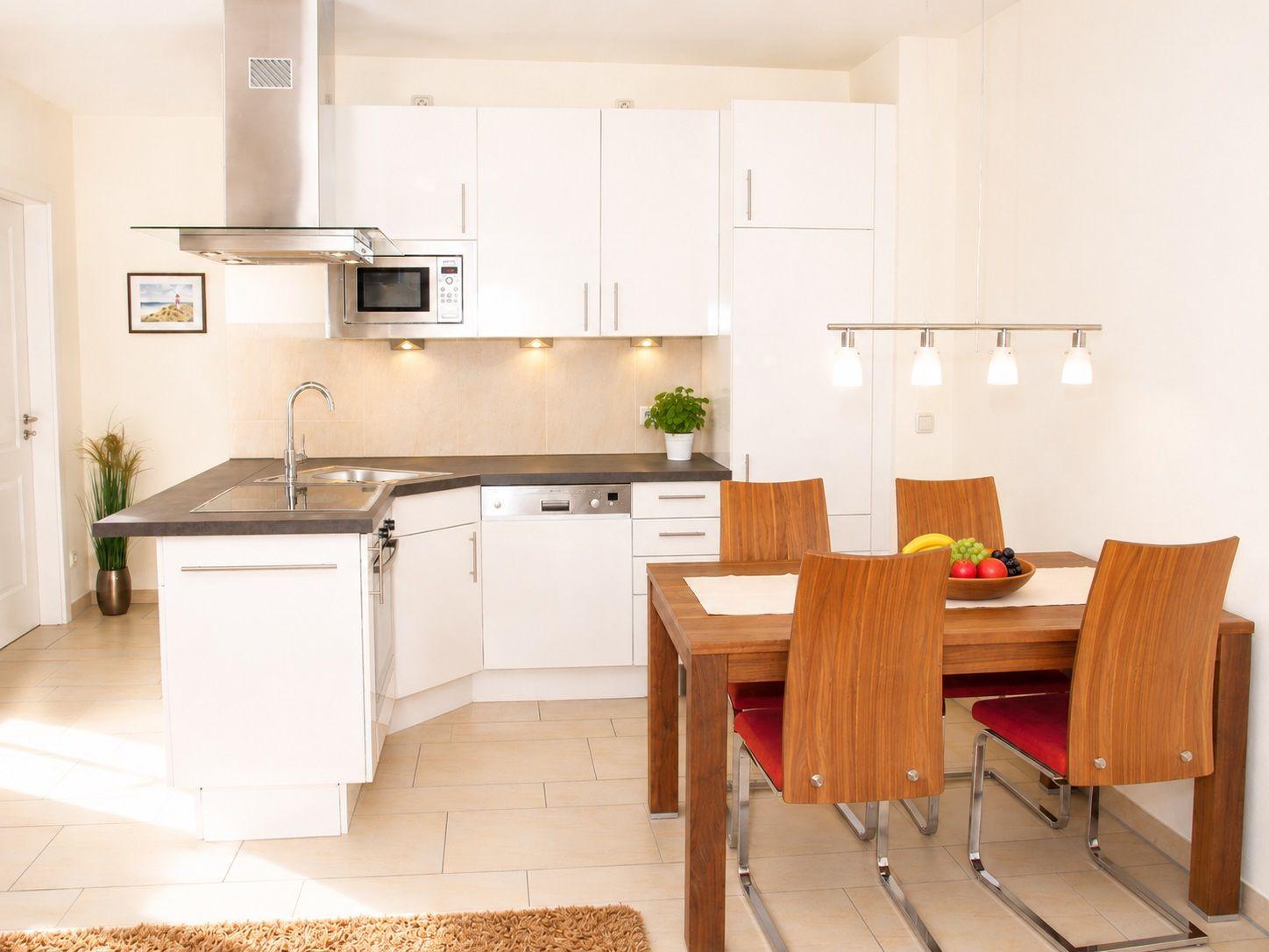 Küche mit Essbereich, weißer Einbauküche, Holztisch und Stühle mit roten Sitzkissen.