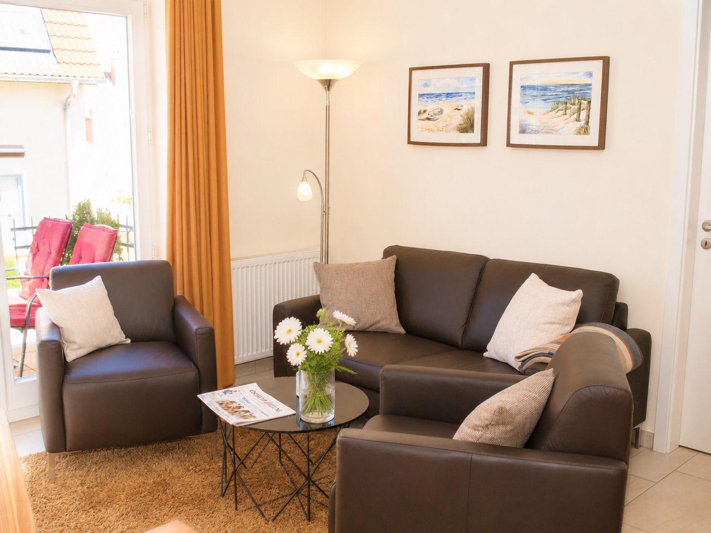 Wohnzimmer mit Sofa, Sessel und Tisch. An der Wand hängen zwei Bilder.
