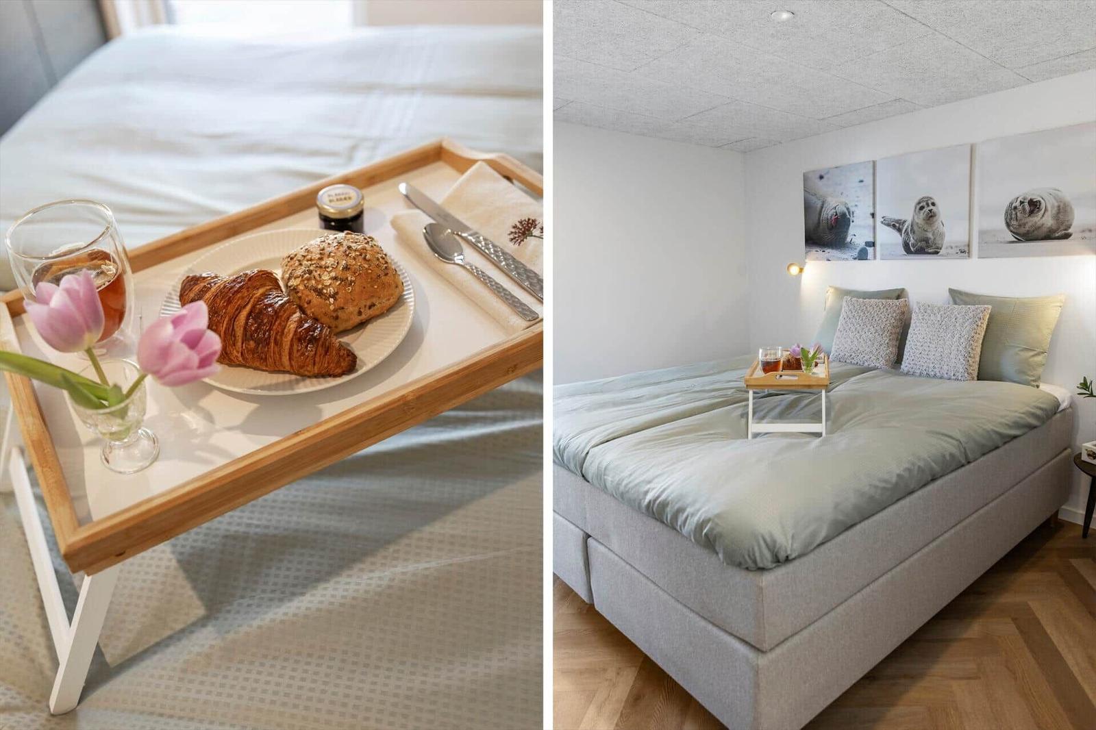 Frühstückstablette mit Brötchen und Blumen auf Bett. Schlafzimmer mit Wandbildern von Seehunden.