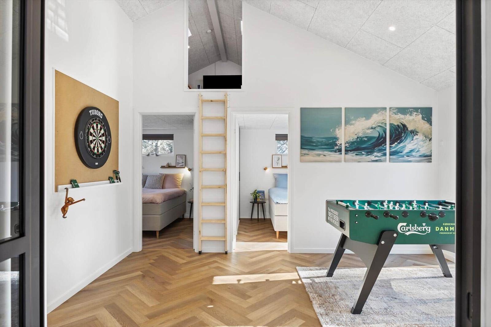 Wohnbereich mit Foosballtisch, Dartboard und Blick in Schlafzimmer. Holzfußboden und Wandbild mit Wellen.