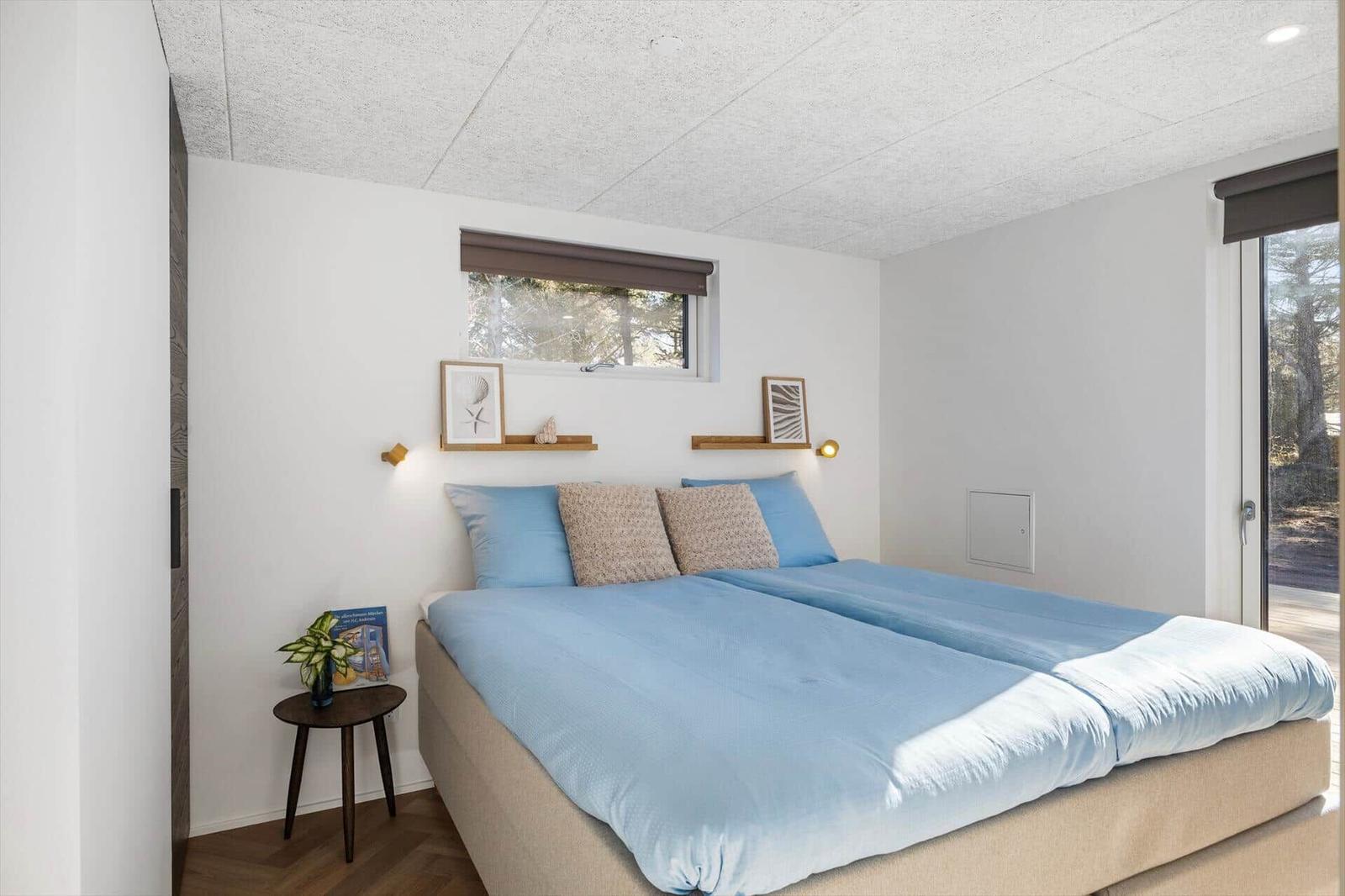Schlafzimmer mit Bett, Fenster und Schiebetür. Wandregale und kleine Tischlampe.