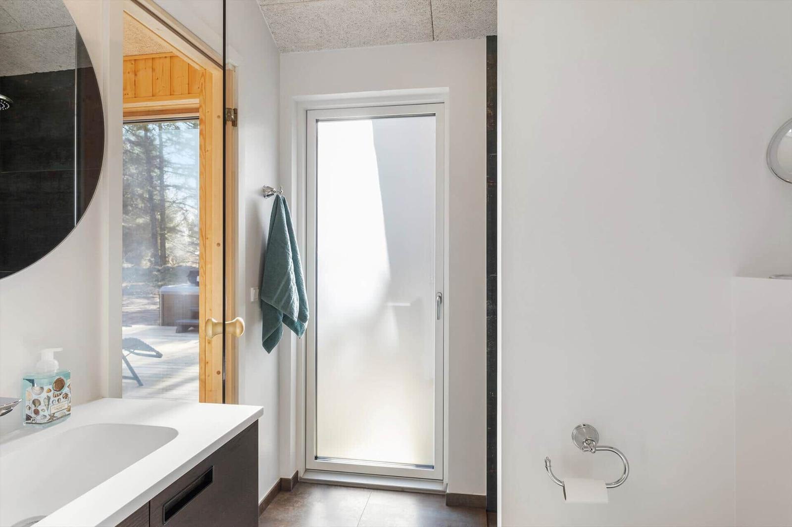 Badezimmer mit Waschbecken, Spiegel und Tür zum Außenbereich.