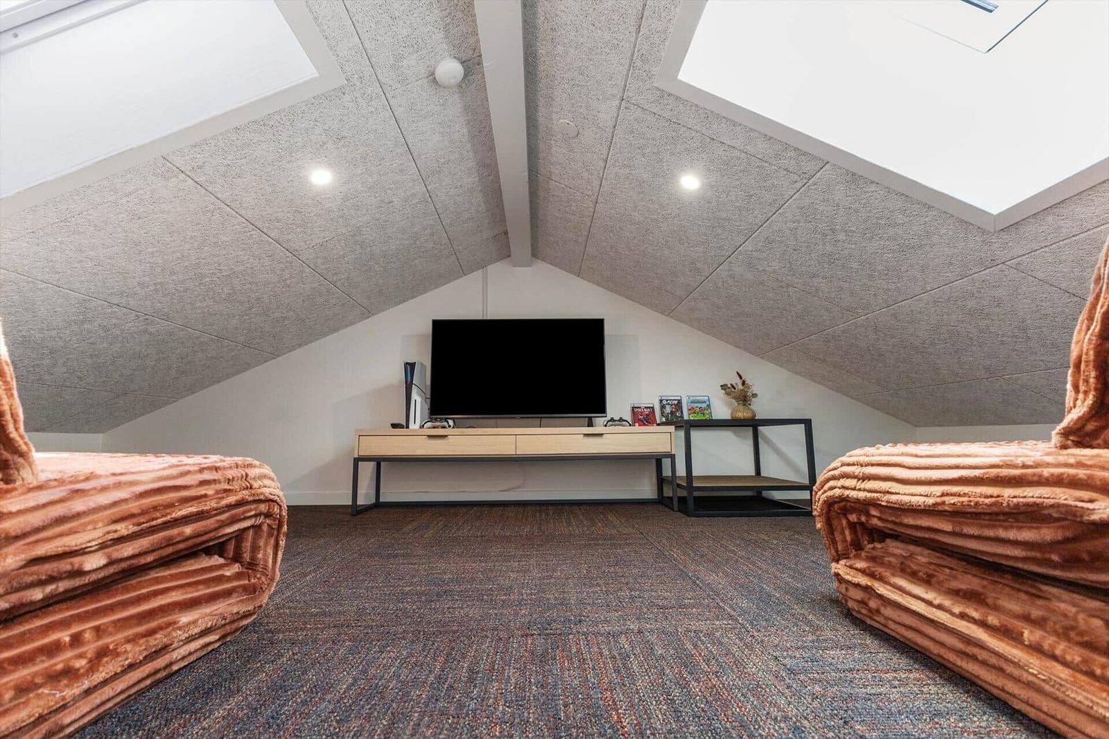 Zimmer mit Dachschrägen, TV und zwei braunen Sofas auf Teppichboden.