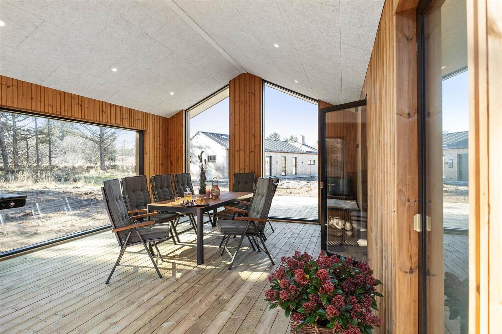 Terrasse mit Esstisch und Stühlen, Holzboden und großflächigen Fenstern zur Aussicht.