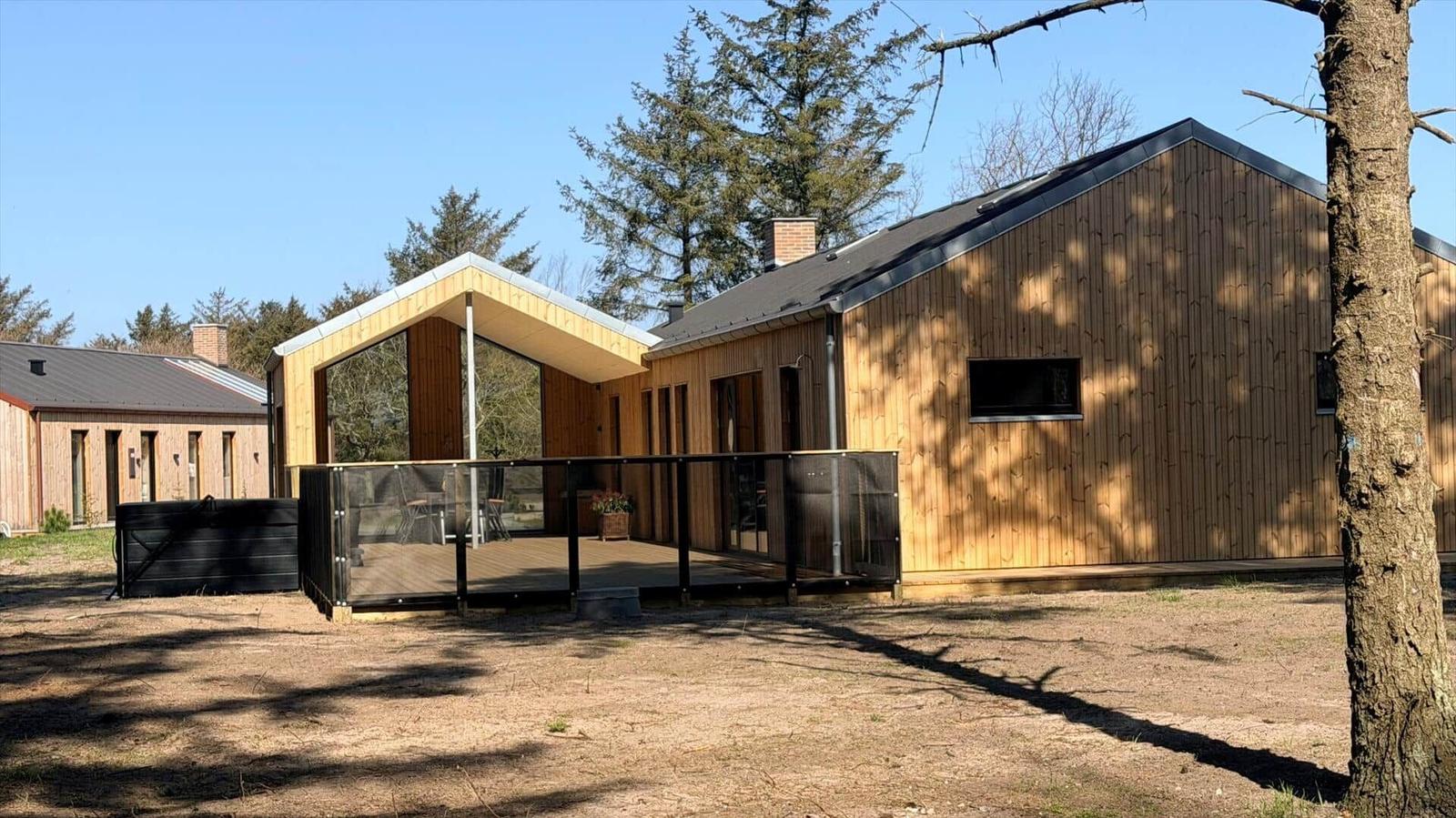 Moderne Holzhütte mit Terrasse und Garten. Umgeben von Bäumen und klarer Luft.