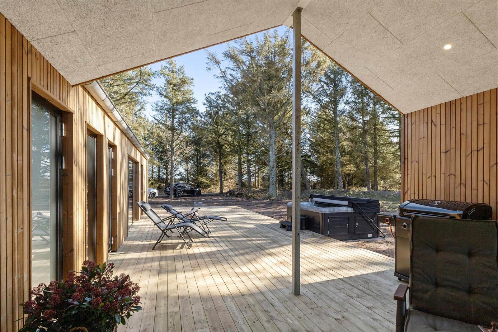 Terrasse mit Holzboden, Liegestühlen, Whirlpool und Grill unter Dach.