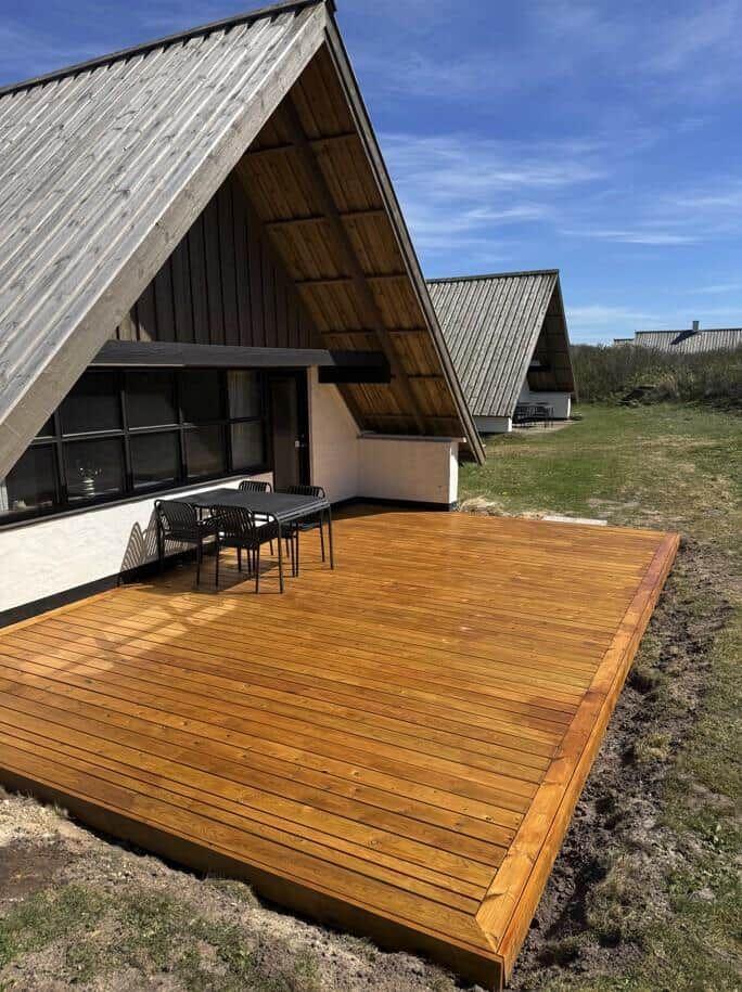 Holzterrasse mit Tisch und Stühlen vor einem A-Fachhaus mit Schiebetüren.