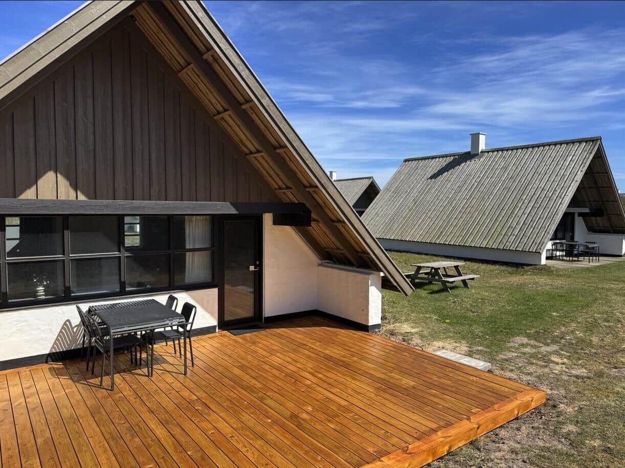 Holzterrasse mit Tisch und Stühlen vor einem A-Fachhaus mit großem Fenster.