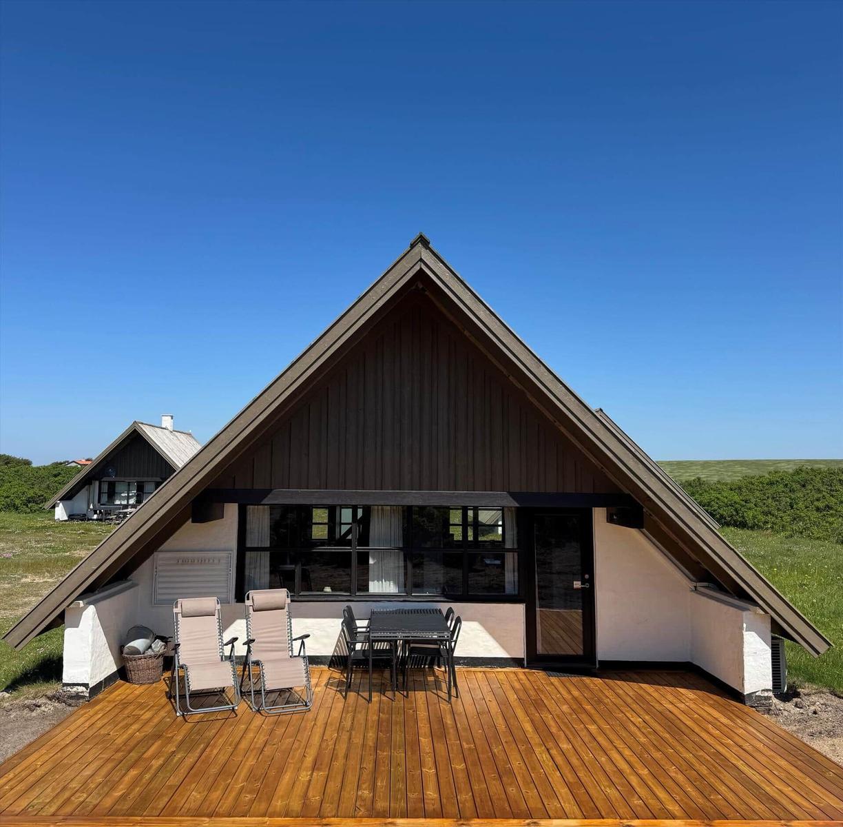 Holzterrasse mit Sitzgelegenheiten vor einem A-Frame-Haus mit großem Fensterbereich.