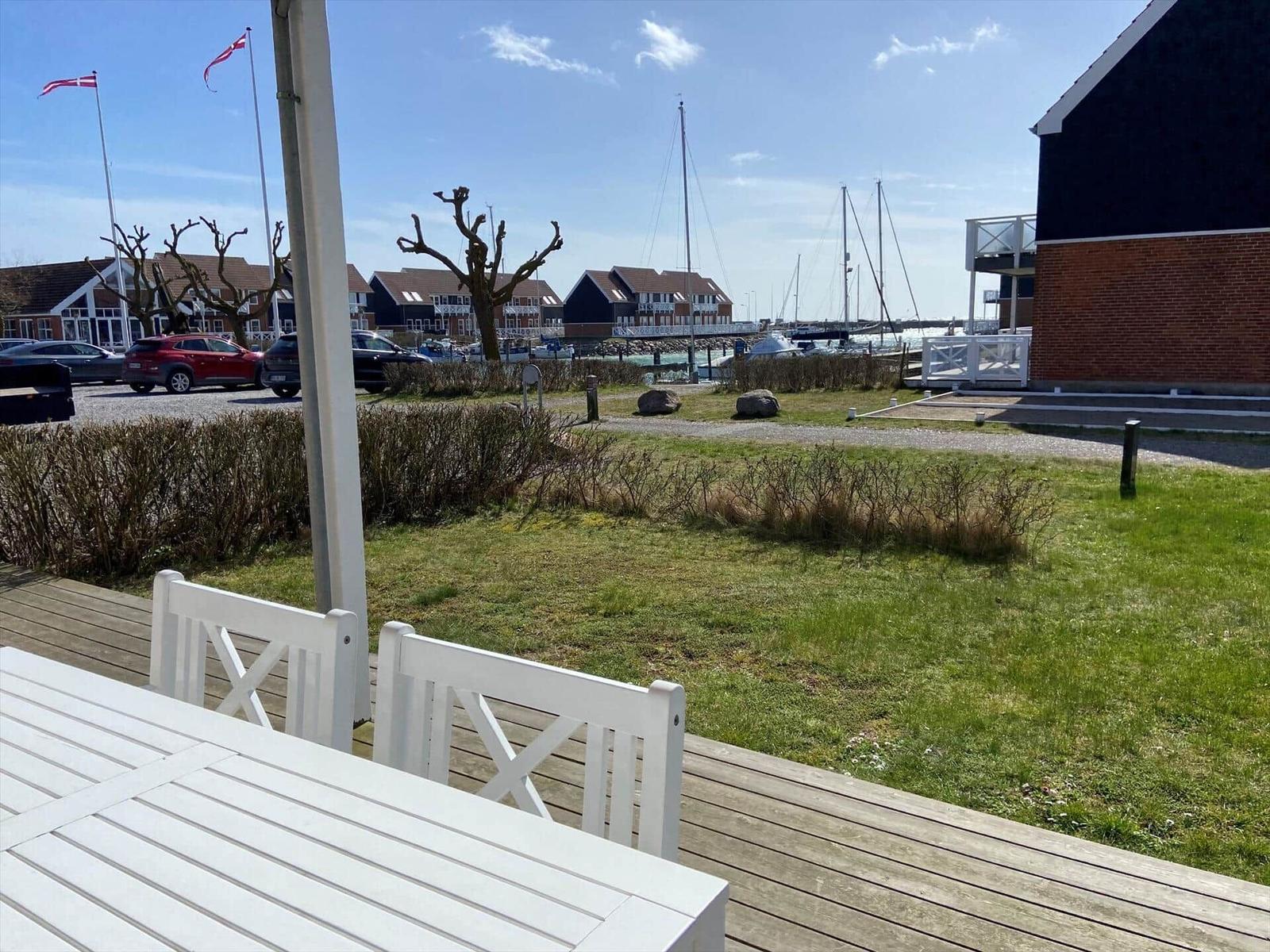 Terrasse mit weißem Tisch und Stühlen. Blick auf Hafen mit Booten und Wohnhäusern.