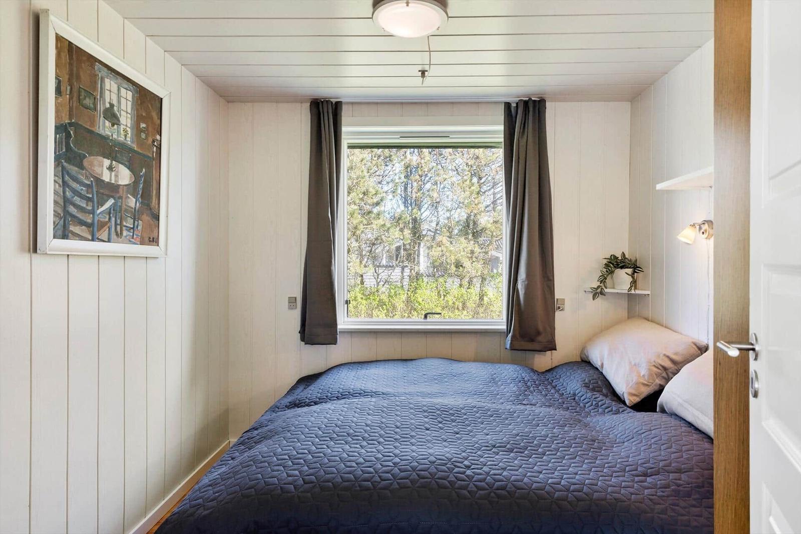 Schlafzimmer mit Bett, Fenster und Wandbild. Holzwandverkleidung und Deckenleuchte.