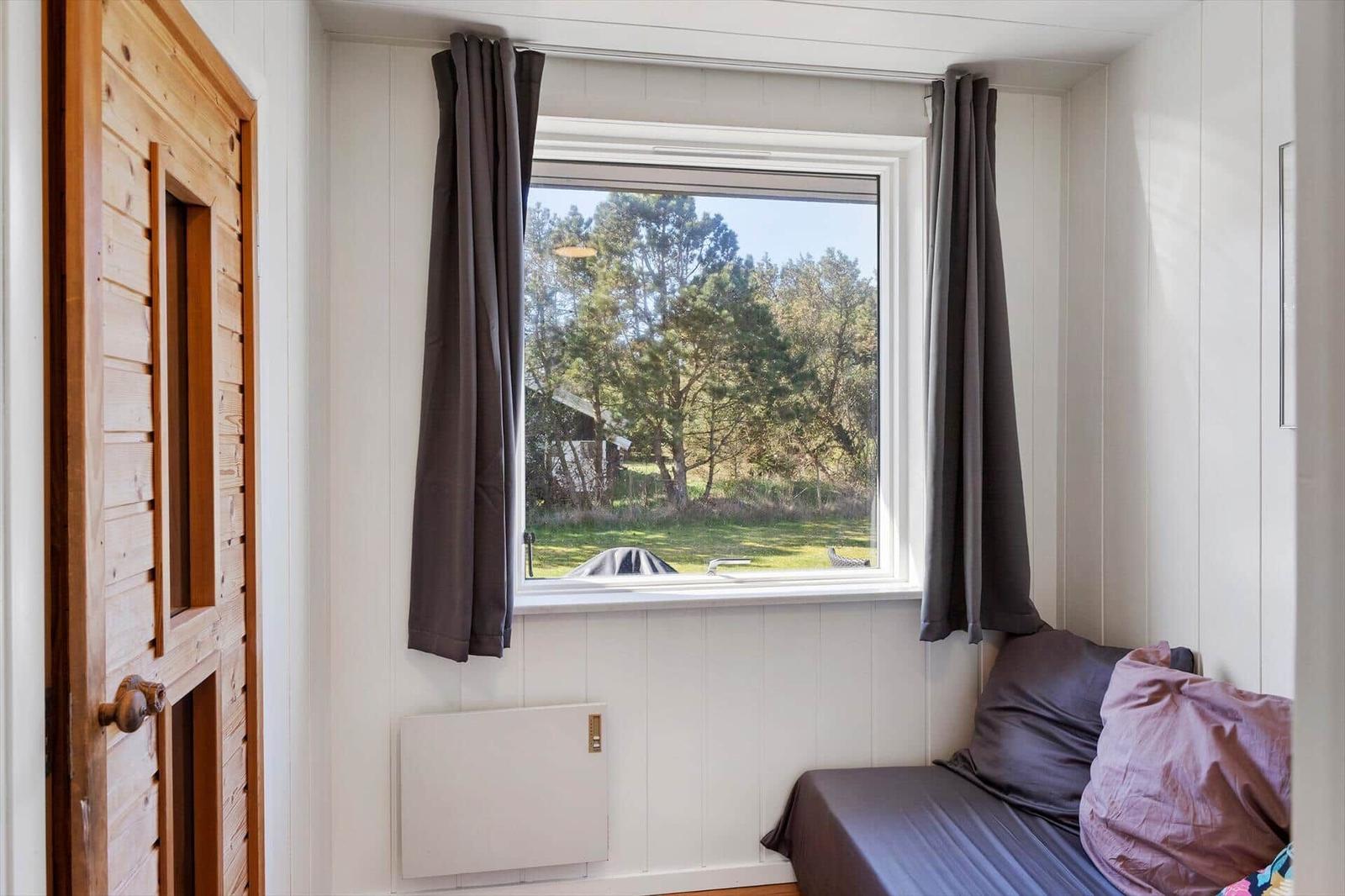 Ein Schlafzimmer mit Fenster, Vorhängen und Bett. Holztür und Heizung sind sichtbar.