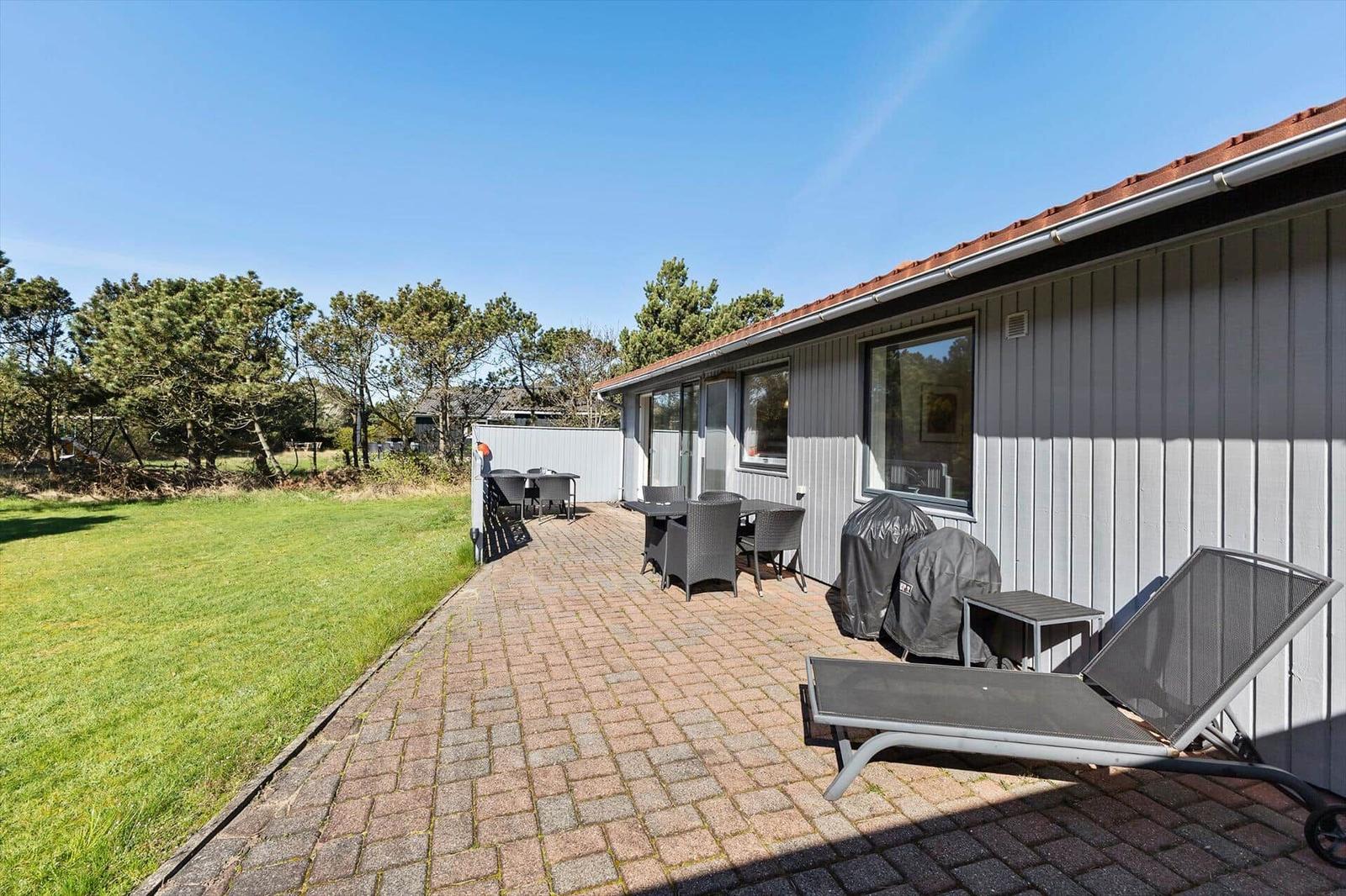 Terrasse mit Garten, Liegestühlen und Tisch. Haus mit Holzfassade und Dach.