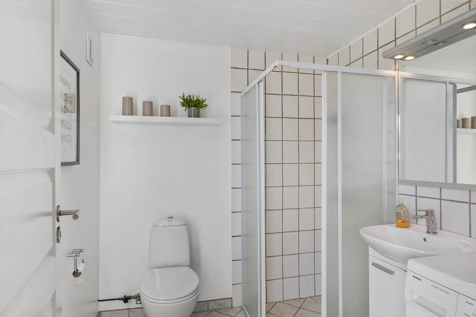 Badezimmer mit Dusche, Waschbecken und Toilette. Weiße Fliesen und Spiegelschrank.
