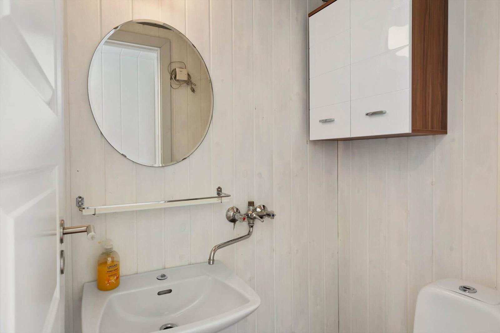 Badezimmer mit Waschbecken, Spiegel und Aufbewahrungskasten an der Wand.