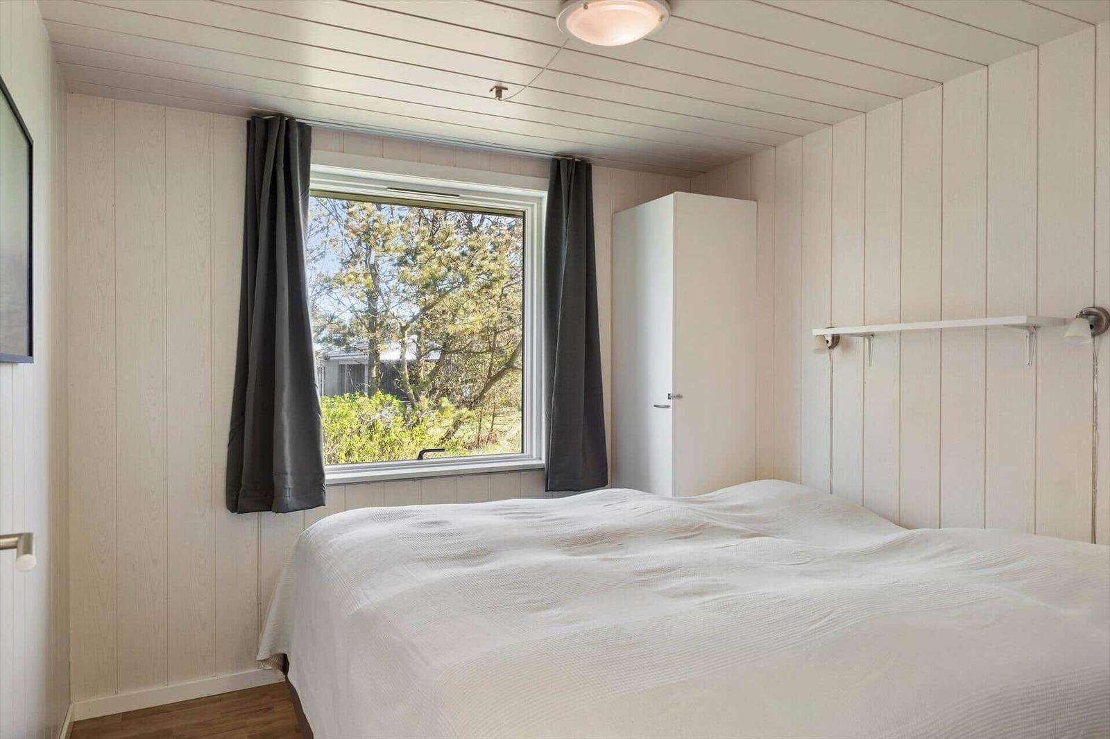 Schlafzimmer mit Bett, Fenster und Schrank. Wandverkleidung und Holzboden.
