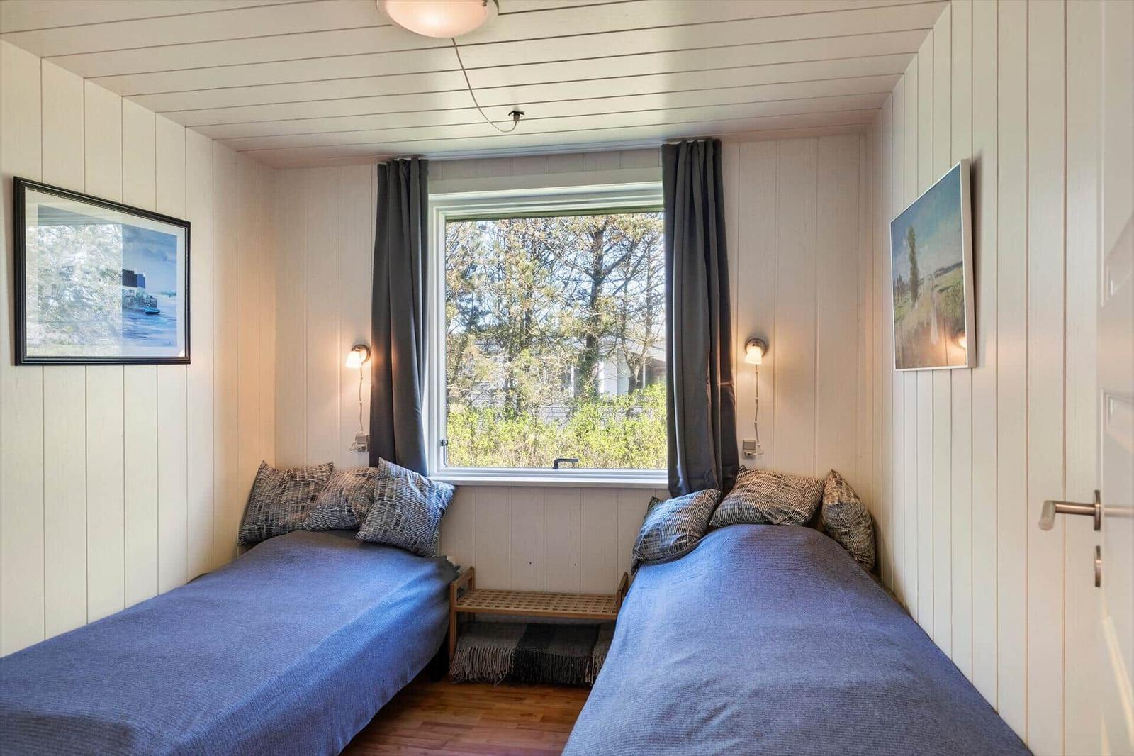 Zwei Einzelbetten mit blauen Bettwäschen, Fenster mit Blick auf Bäume und Wandbilder.