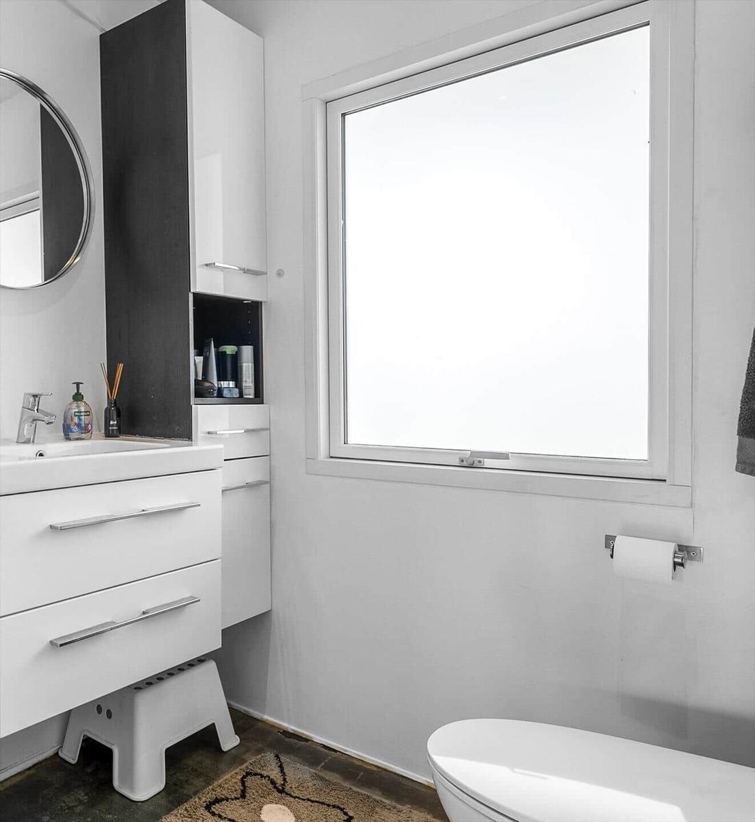 Badezimmer mit Waschbecken, Spiegel, Fenster und Toilette.