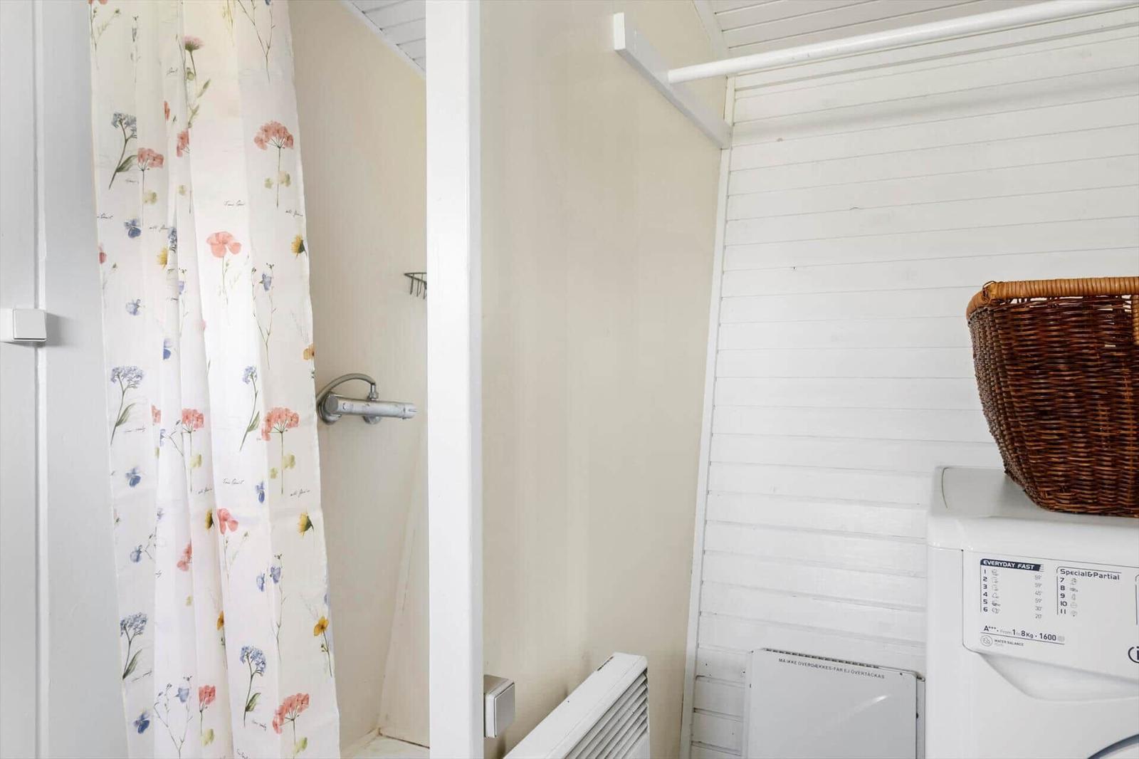 Shower with floral curtain and washing machine with basket.