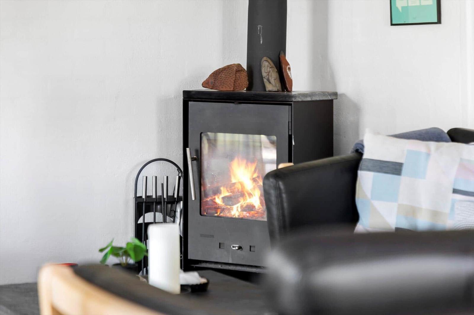 A wood-burning stove with fire, next to a sofa with cushions.