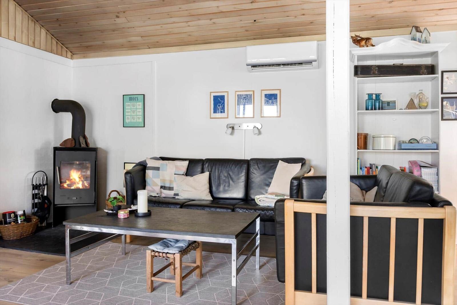 Living room with sofa, fireplace, and table. Shelf and ceiling made of wood.