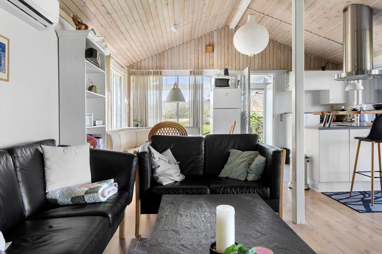 Living area with black leather sofas, wooden floor, and kitchen area in the background.
