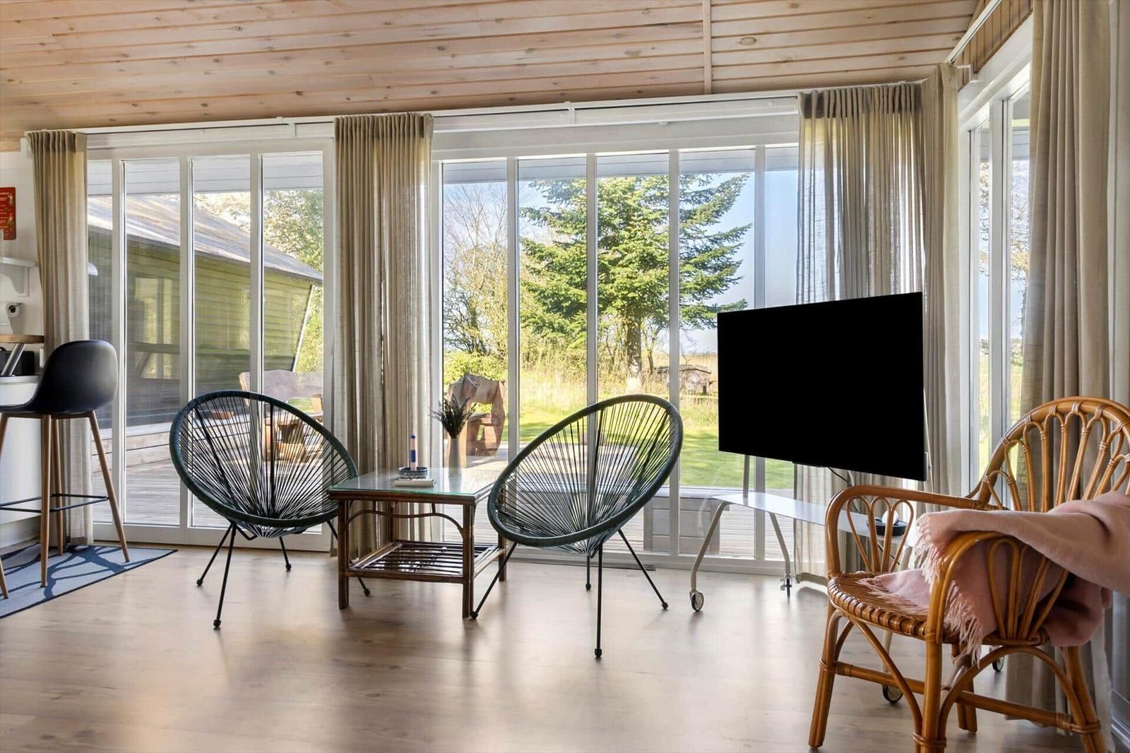 A living room with large windows, two chairs, and a TV.