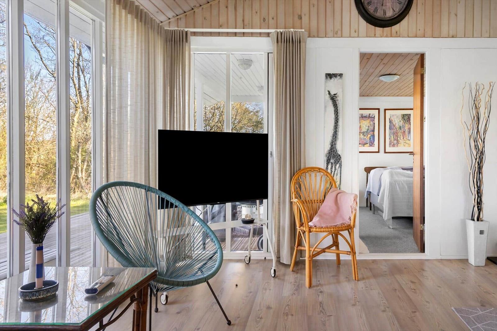 Living room with TV, chairs, and view to balcony. Bedroom visible in background.