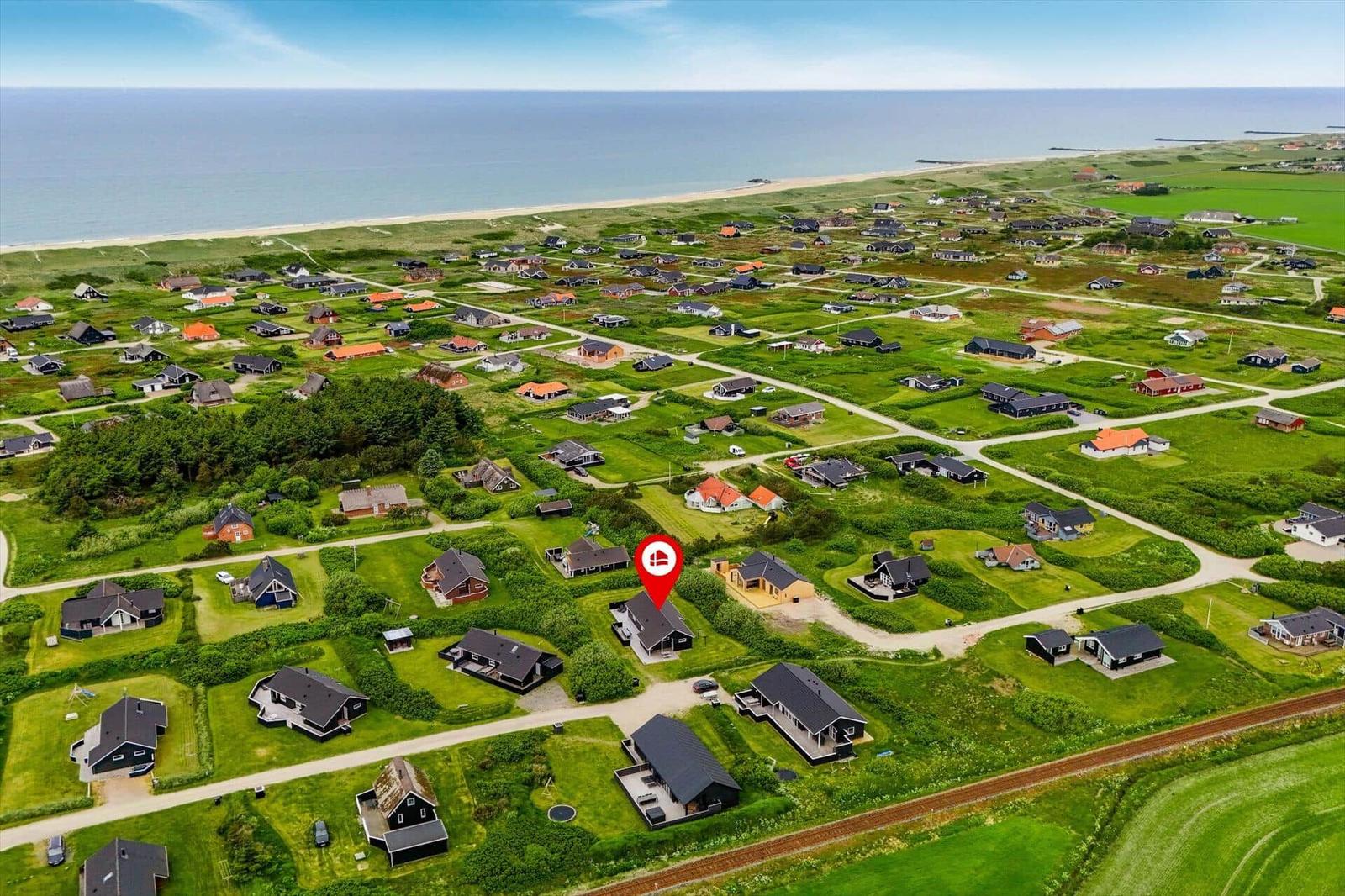 Luftbild von Ferienhäusern an der Küste mit grünen Wiesen und Strand.