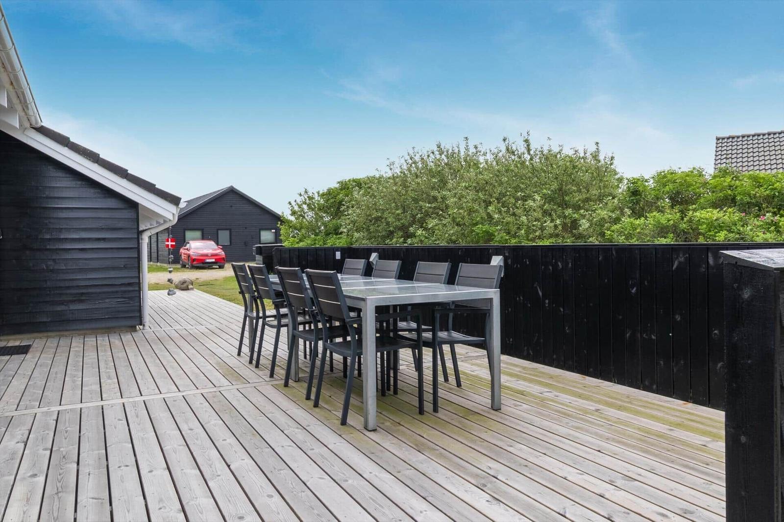 Terrasse mit Tisch und Stühlen, umgeben von schwarzer Holzabtrennung und grüner Vegetation.