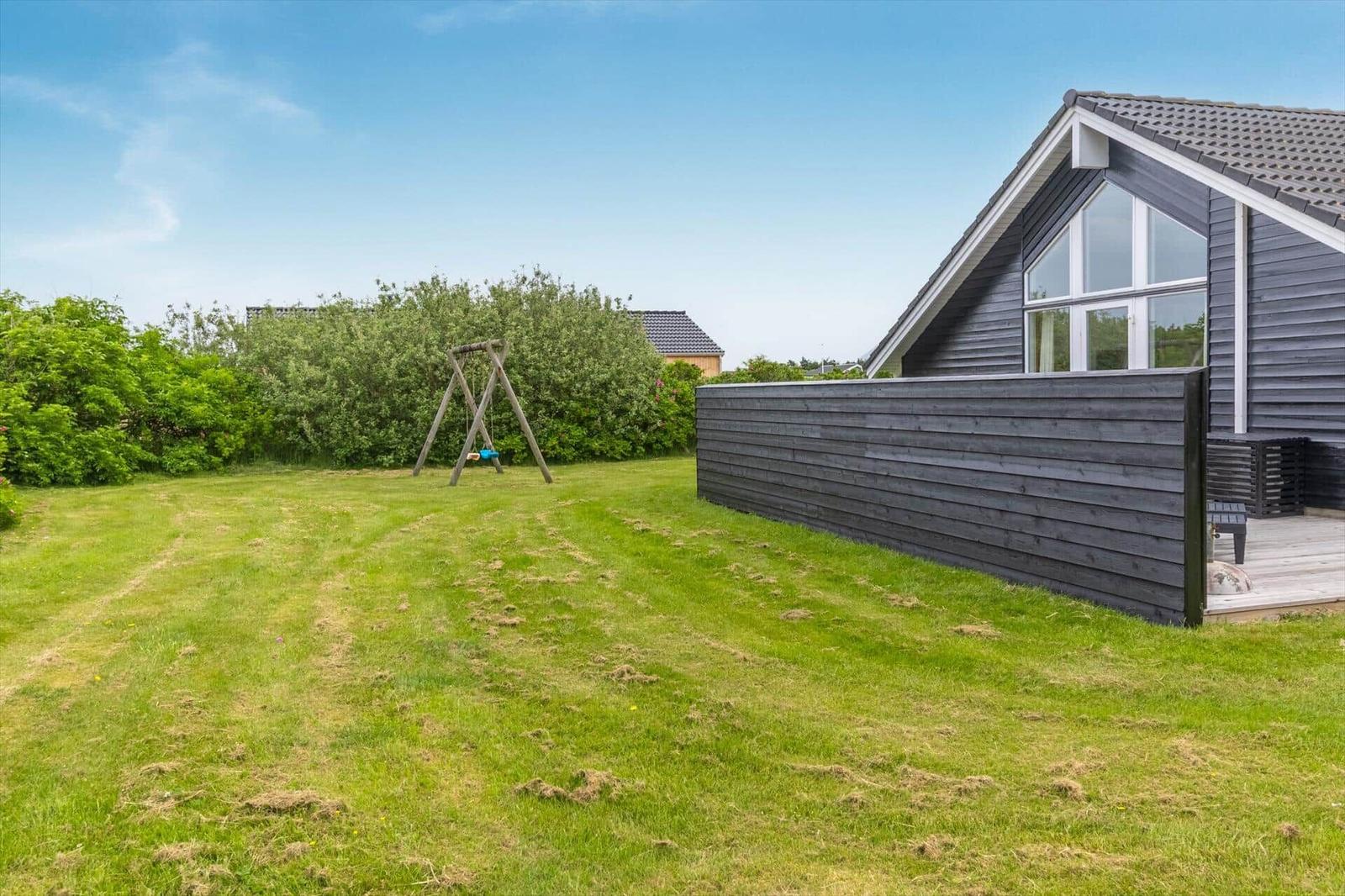 Hinterhof mit Grasfläche, Spielgeräte und modernem Haus mit Holzverkleidung.