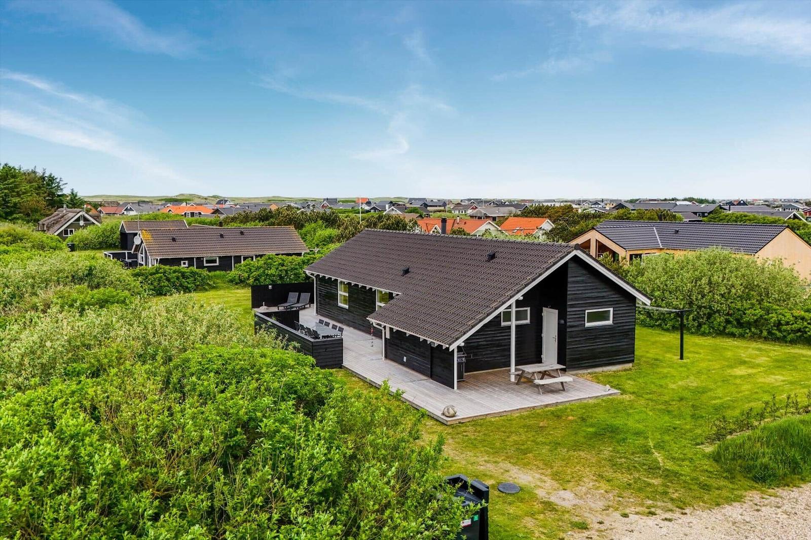 Schwarzes Holzhaus mit Terrasse und Garten. Blick auf Wohnsiedlung im Hintergrund.