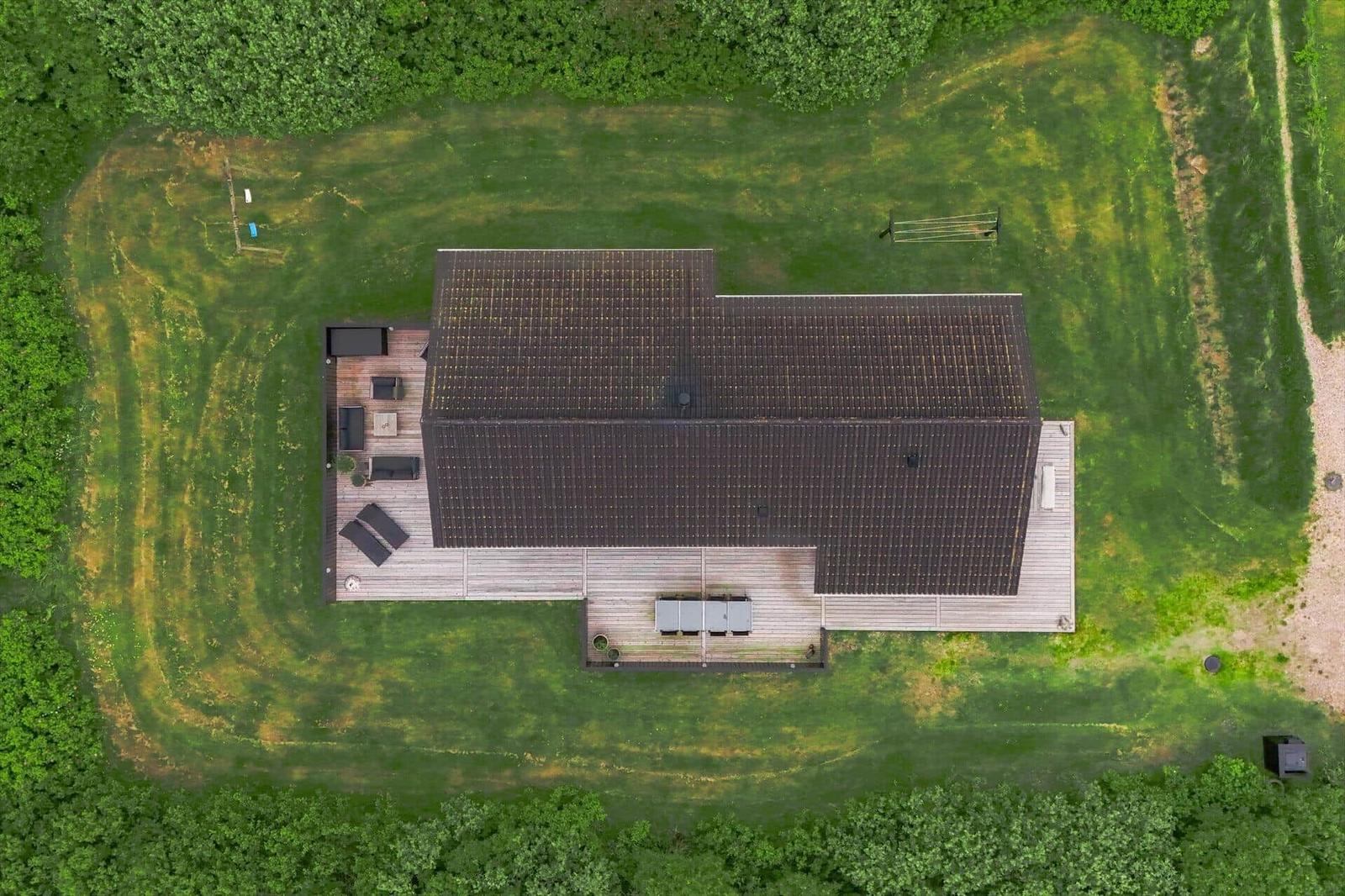 Haus mit Holzterrasse und Garten, umgeben von Wald. Pool und Liegestühle sichtbar.