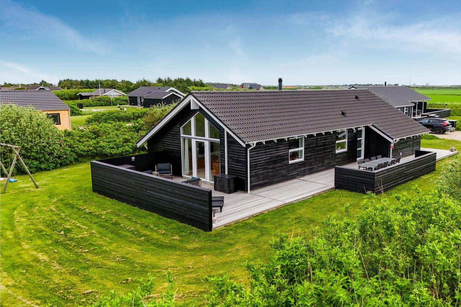 Moderne Holzhütte mit Terrasse und Garten. Große Fensterfront. Schwarze Fassade.