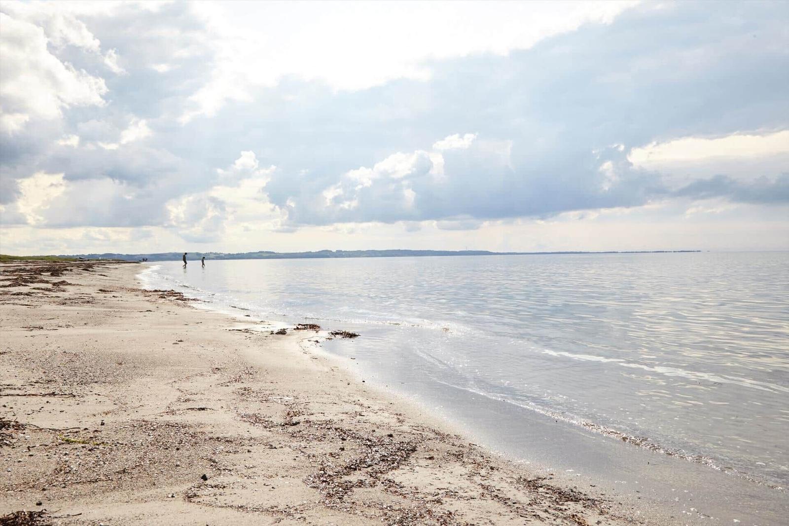 Beach with gentle waves and two people in the water under a cloudy sky.