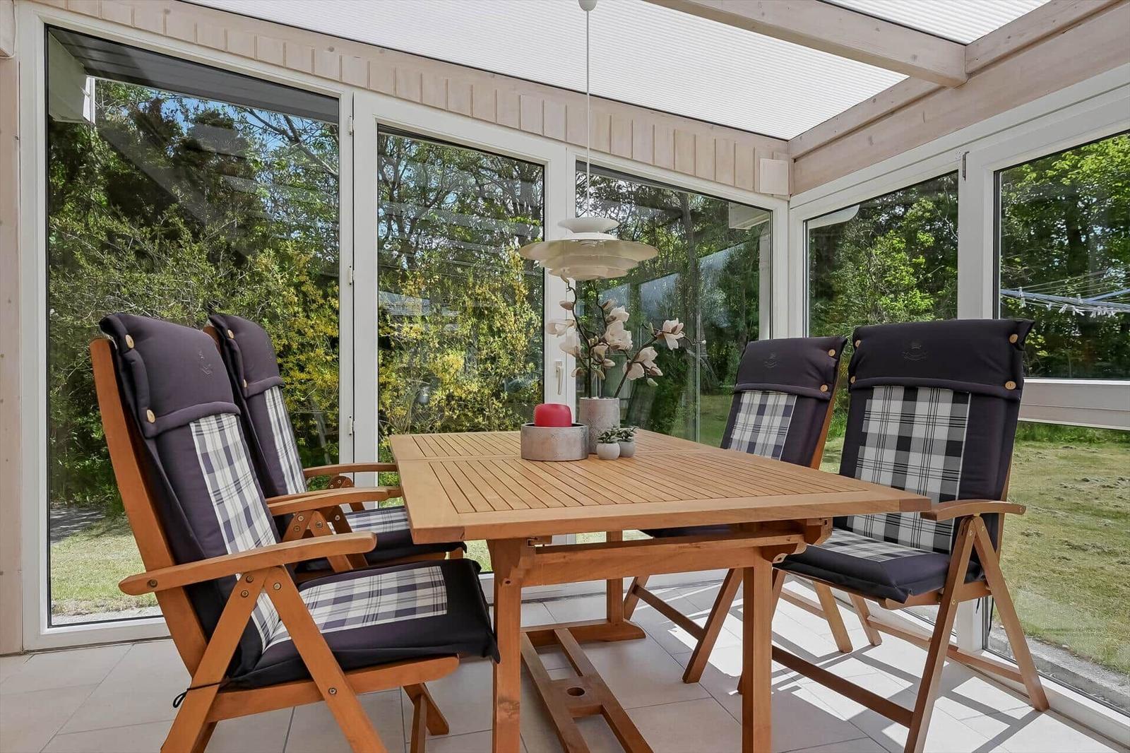 Holztisch mit vier Stühlen und Plaidbezug im Innenhof mit Glaswänden.
