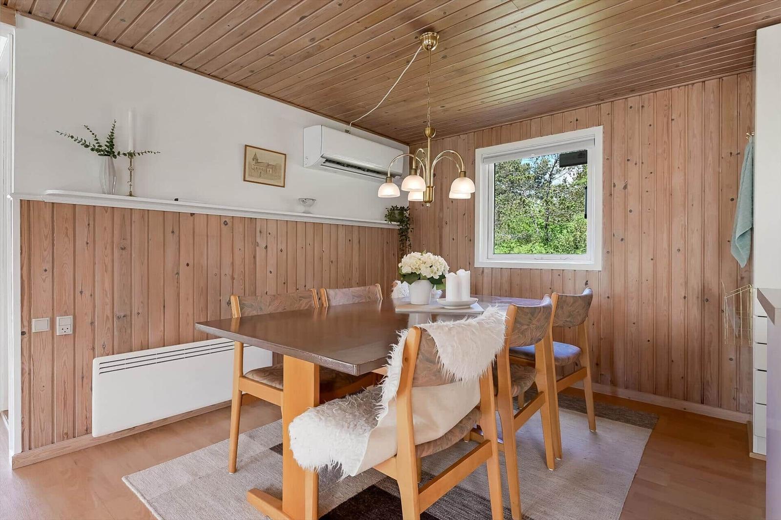 Esszimmer mit Holzwand, Tisch, Stühlen und Fenster zum Garten.