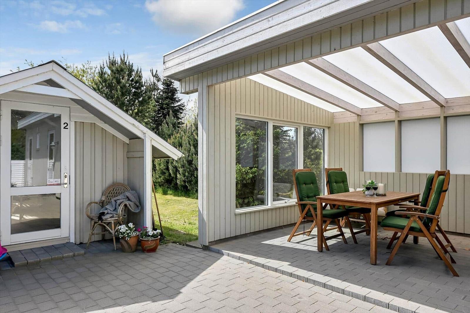 Terrasse mit Tisch und Stühlen unter Markise. Neben dem Eingang mit Pflanzen.