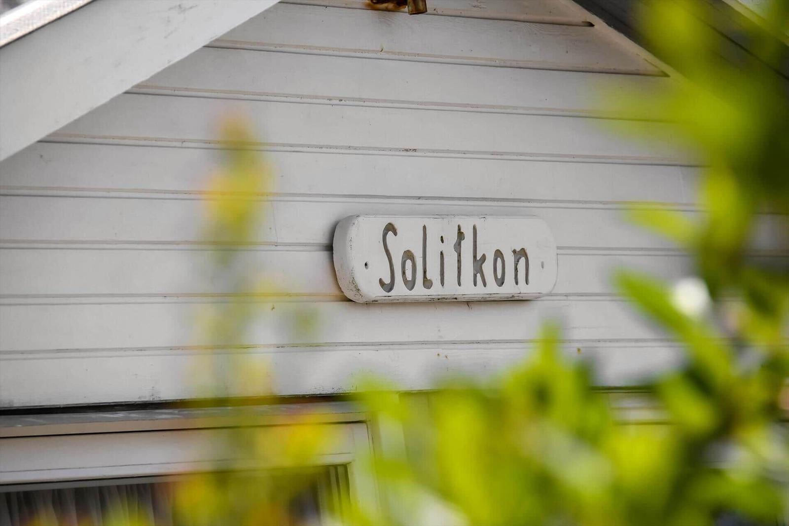 Schild mit der Aufschrift Solitkon an einer weißen Hauswand, teilweise von Pflanzen verdeckt.