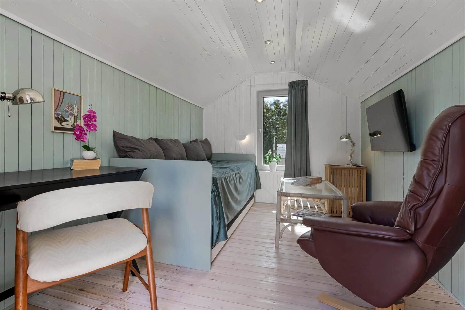 Schlafzimmer mit Bett, Schreibtisch, Sessel und Fernseher an der Wand.
