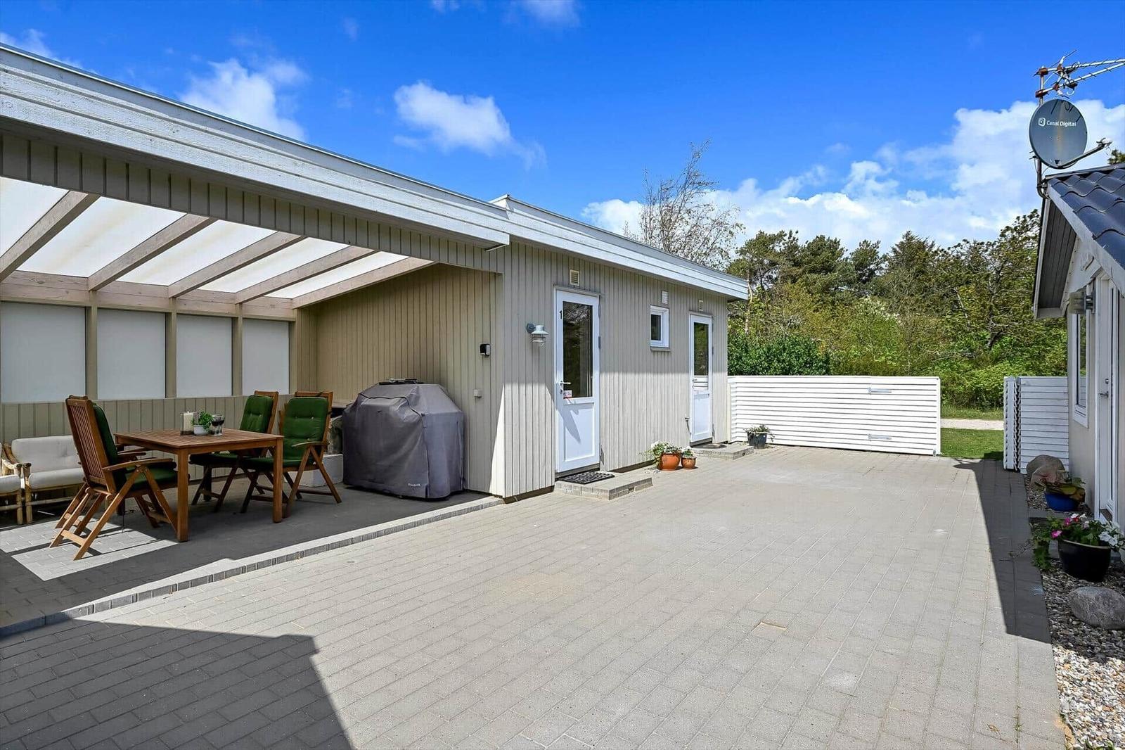 Haus mit überdachter Terrasse, Grill und Pflanzen im Garten.