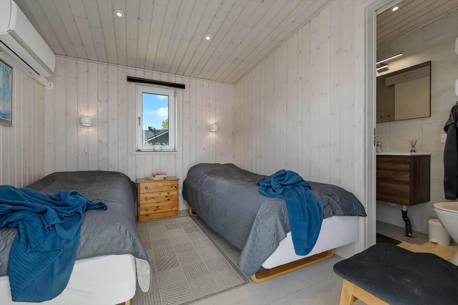 Zwei Betten, Fenster, Nachttisch, Bad mit Waschbecken und Toilette.