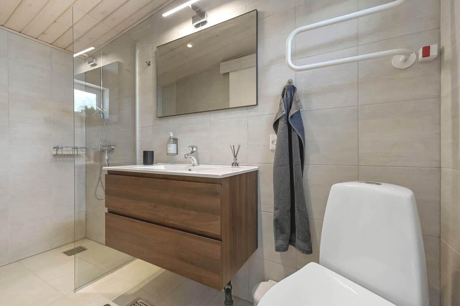 Bad mit Dusche, Waschbecken und Toilette. Wandhalterung und Spiegel sichtbar.